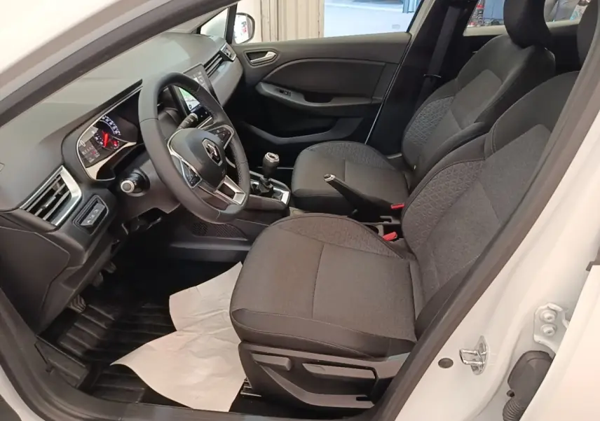 Vue intérieure côté conducteur d'une Renault Clio blanche 2020, volant multifonctions cuir et sièges tissu gris.