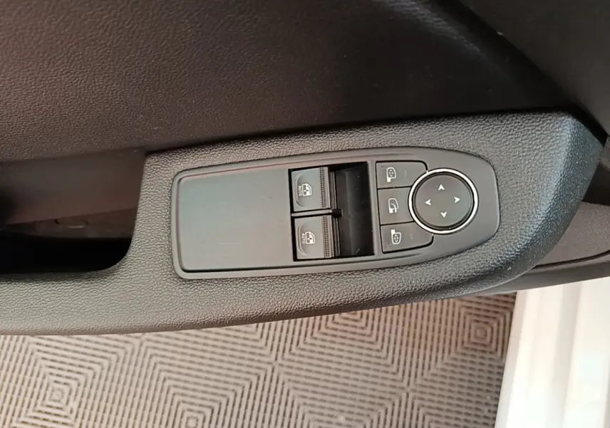 Gros plan sur les commandes de lève-vitres et rétroviseurs côté conducteur d'une Renault Clio blanche, intérieur noir.