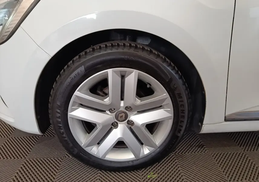 Gros plan sur la roue avant droite d'une Renault Clio blanche, jante alliage à cinq branches doubles.