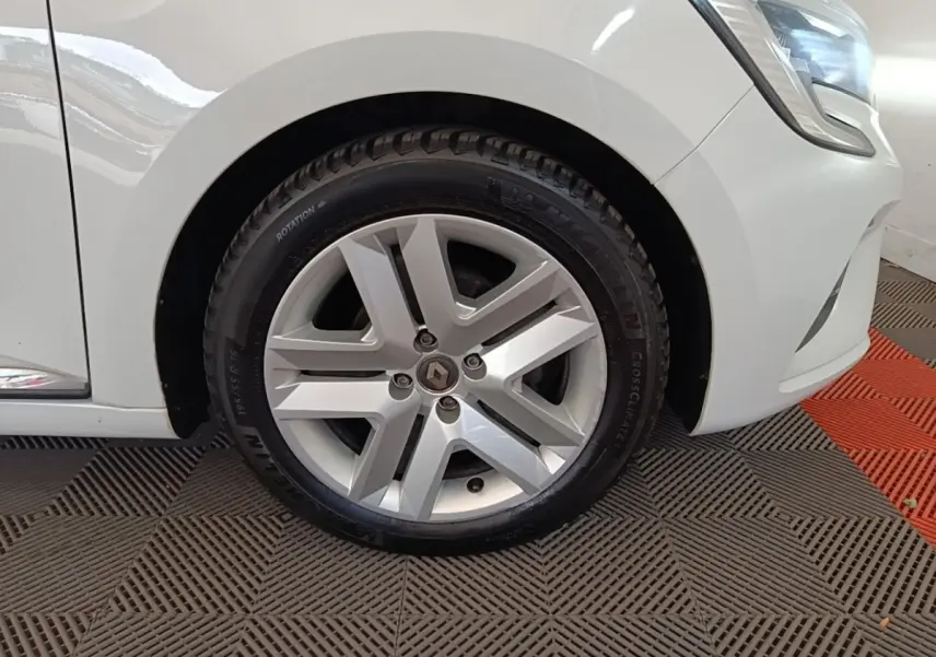 Gros plan sur la roue avant droite d’une Renault Clio blanche 2020 avec jante alliage et partie du phare avant visible.