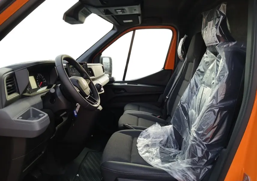 Vue intérieure côté conducteur du Renault Master orange 2026, montrant le tableau de bord et les sièges avant protégés par des housses plastiques.