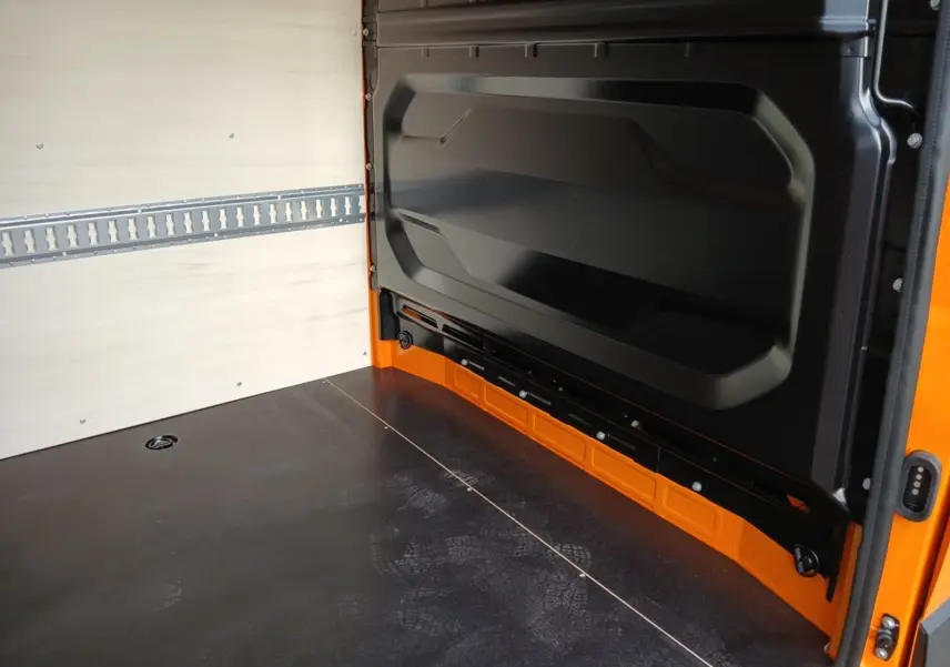 Intérieur de la zone de chargement du Renault Master orange, vue depuis l'arrière avec parois en bois clair et sol noir.