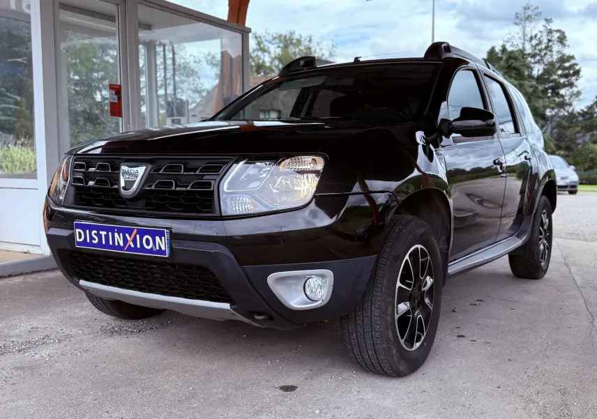 Dacia Duster noir métal vu en 3/4 avant droit, mettant en valeur sa calandre distinctive et ses jantes bi-ton.