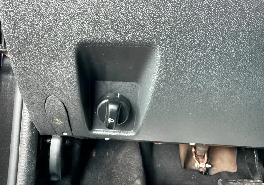 Gros plan sur le bouton de réglage des phares sous le tableau de bord d'un Dacia Duster noir métal.