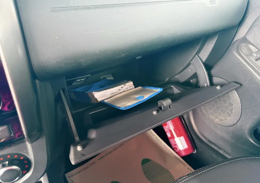 Gros plan sur la boîte à gants ouverte du Dacia Duster noir métal, montrant des documents et un extincteur rouge.