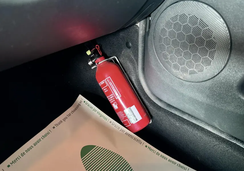 Extérieur noir métal non visible, image montrant un extincteur rouge fixé sous le tableau de bord côté passager du Dacia Duster.