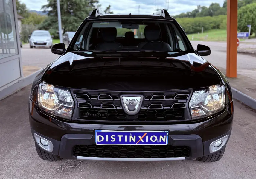 Vue de face du Dacia Duster noir métal 2017 avec calandre noire et phares allumés sous abri.