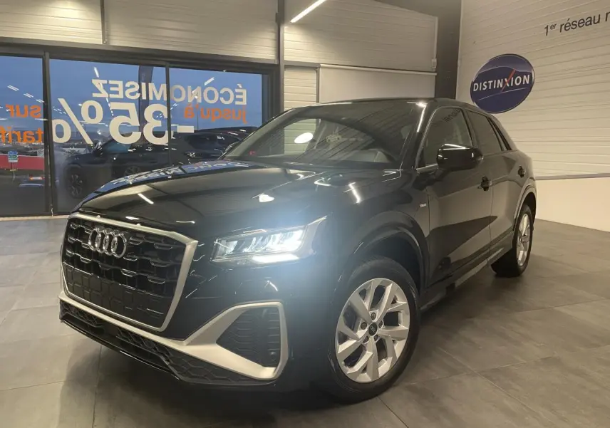 Audi Q2 noir métallisé vue 3/4 avant droit en intérieur, avec phares LED allumés et jantes alliage visibles.