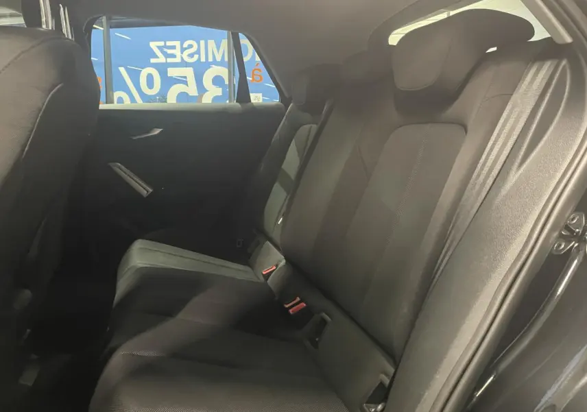 Vue intérieure du siège arrière droit de l'Audi Q2 noir métallisé, avec sellerie tissu et ceinture de sécurité visible.