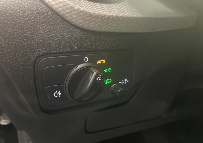 Gros plan sur la commande d’éclairage intérieure noire de l’Audi Q2, avec réglage rotatif et indicateurs lumineux verts et jaunes.