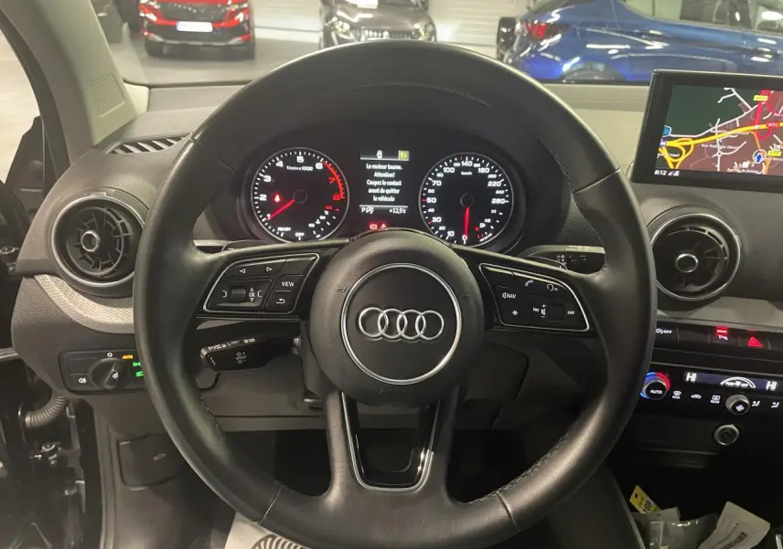 Vue intérieure centrée sur le volant cuir noir de l'Audi Q2 2023 avec tableau de bord et écran de navigation visibles.