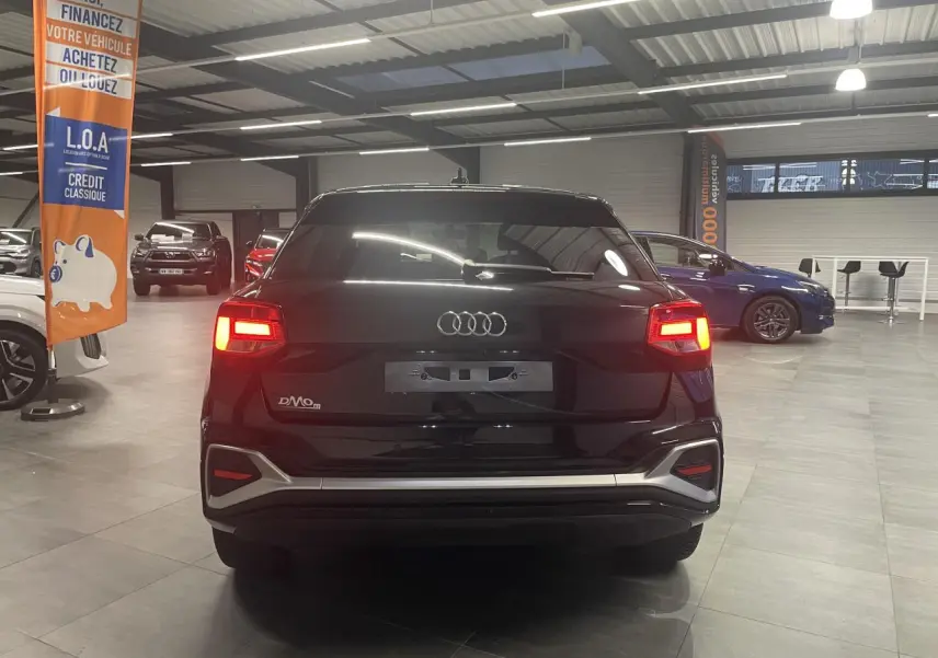 Vue arrière d'un Audi Q2 noir métallisé 2023 avec feux LED allumés dans un showroom.