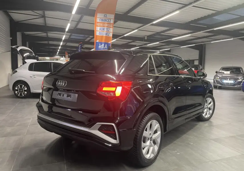 Vue 3/4 arrière droit d’un Audi Q2 noir métallisé avec feux arrière LED allumés en intérieur showroom.
