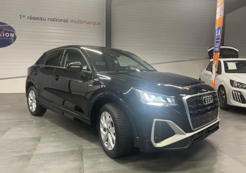 Audi Q2 noir métallisé vue 3/4 avant droit avec phares allumés dans un showroom intérieur.