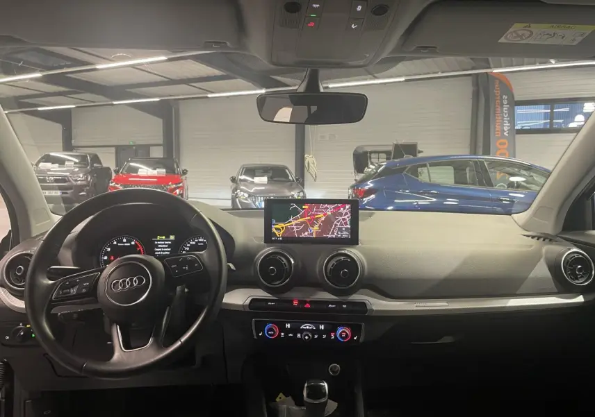 Vue intérieure avant de l'Audi Q2 2023 avec tableau de bord noir, volant multifonction et écran central de navigation allumé.