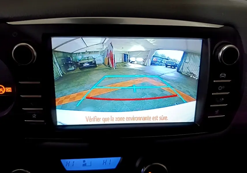 Vue de l'écran de caméra de recul de la Toyota Yaris blanche, affichant les lignes de guidage dans un garage.