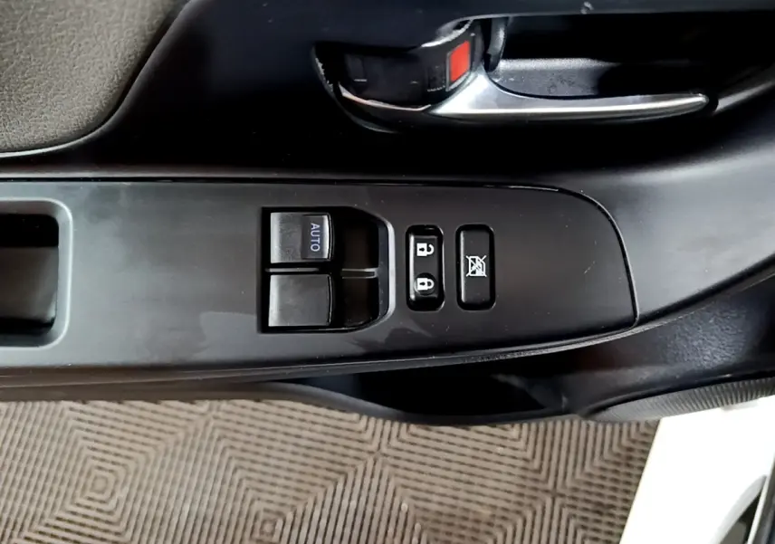 Gros plan sur les commandes de porte côté conducteur d'une Toyota Yaris blanche, avec boutons de verrouillage et lève-vitres.