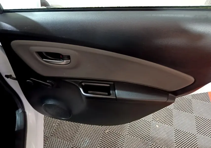 Vue intérieure du panneau de porte avant gauche de la Toyota Yaris blanche, avec poignée et haut-parleur intégrés.