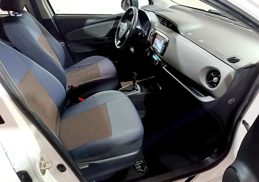 Vue intérieure côté conducteur de la Toyota Yaris blanche 2019, montrant sièges tissu bicolore et tableau de bord avec écran tactile.