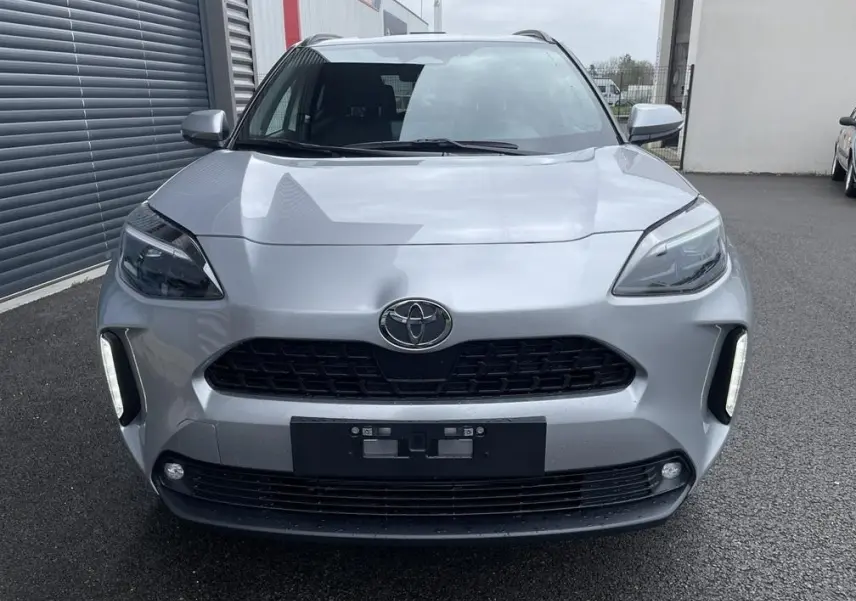Vue frontale d'une Toyota Yaris Cross 1.5 Hybrid gris clair avec calandre noire et feux LED verticaux allumés.