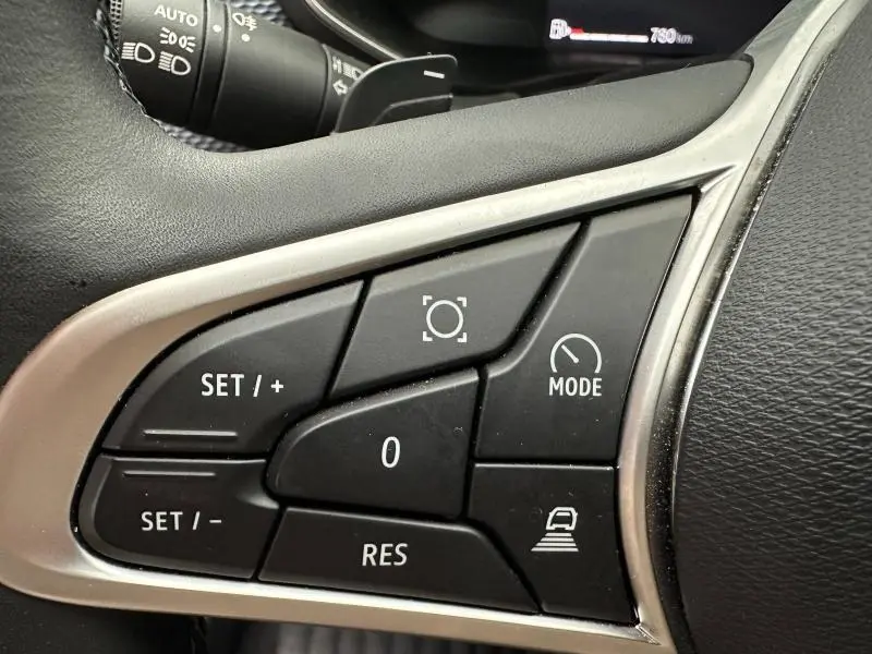 Gros plan sur les commandes au volant du Renault Arkana 2025, boutons noirs avec cadre argenté et affichage partiel du tableau de bord.