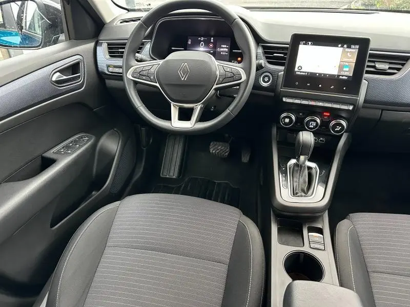 Vue intérieure avant du Renault Arkana 2025, tableau de bord avec écran tactile et volant multifonction, sièges tissu gris.