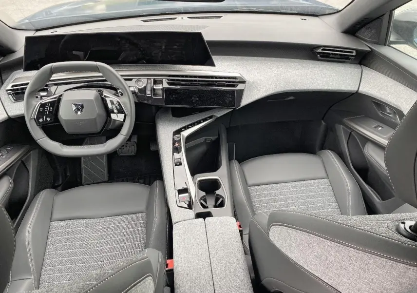 Vue intérieure avant du Peugeot 3008 2025, volant compact, tableau de bord numérique et sellerie gris clair et noir.