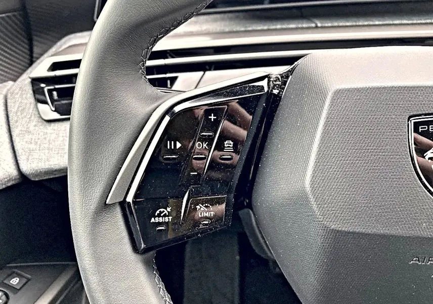 Gros plan sur le côté gauche du volant cuir Peugeot 3008 2025 avec commandes multifonctions et logo central.