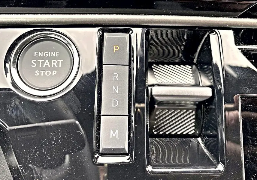 Gros plan sur la console centrale noire brillante du Peugeot 3008 1.2 hybrid 145 allure e-dcs6 avec bouton start/stop et sélecteur de vitesses automatique.