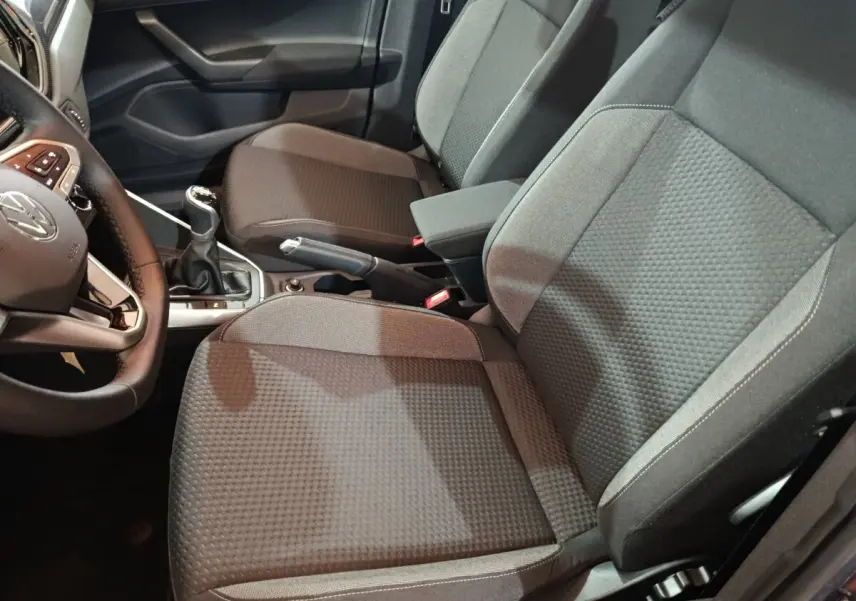 Vue intérieure côté conducteur de la Volkswagen Polo gris foncé 2025, montrant sièges tissu et levier de vitesses manuel.