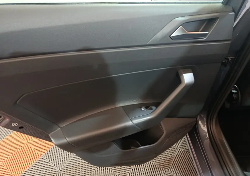 Vue rapprochée de la porte intérieure côté gauche gris foncé de la Volkswagen Polo 2025 avec poignée angulaire et bouton de vitre électrique.