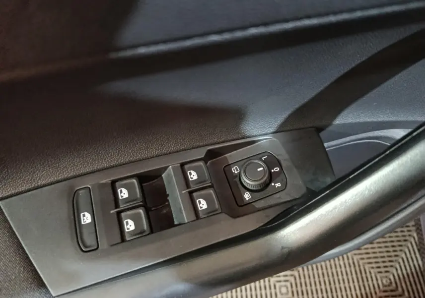 Gros plan sur les commandes de lève-vitres et réglage des rétroviseurs côté conducteur d’une Volkswagen Polo gris foncé.