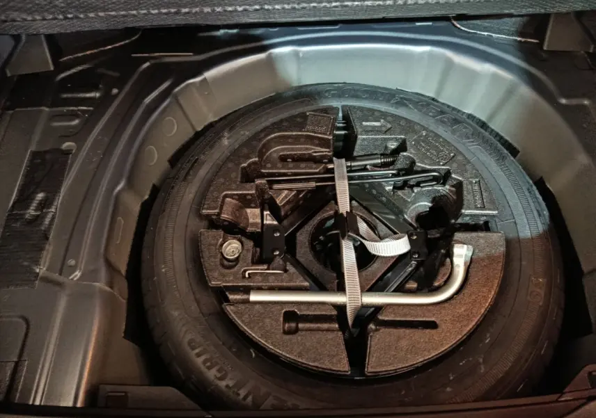 Vue en plongée du coffre d'une Volkswagen Polo gris foncé, montrant la roue de secours et les outils de bord.
