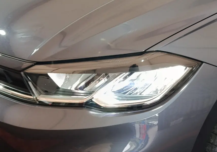 Gros plan sur le phare avant droit allumé d'une Volkswagen Polo gris foncé, mettant en valeur ses lignes modernes.