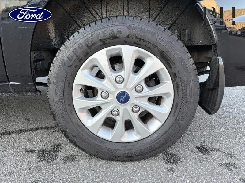 Gros plan sur la roue avant droite du Ford Transit Custom noir Agate métallisé avec jante alu 16 pouces et logo Ford central.