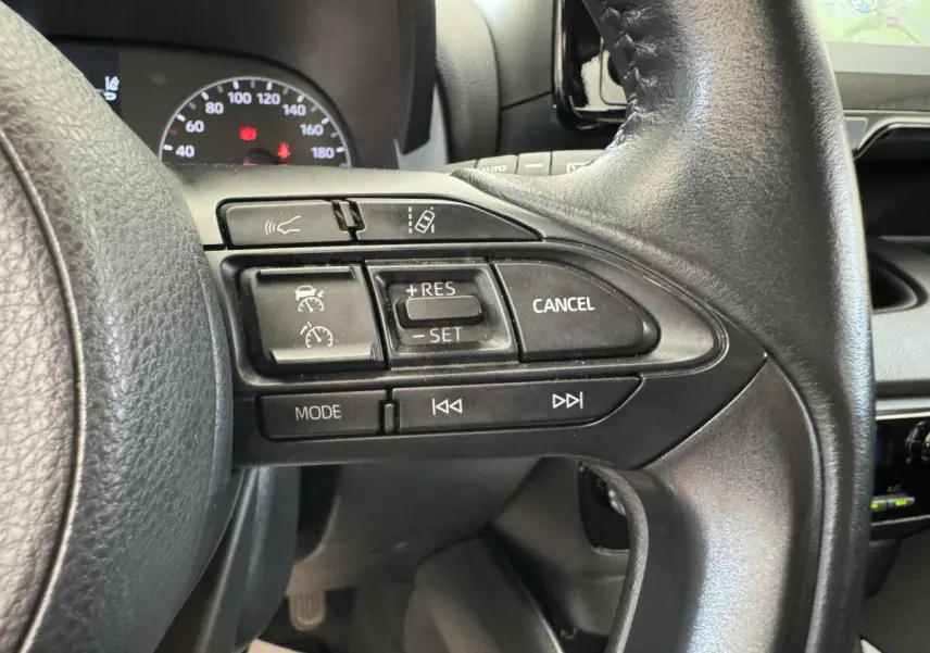 Gros plan sur les commandes au volant en cuir noir de la Toyota Yaris hybride 2022, avec tableau de bord et écran tactile en arrière-plan.