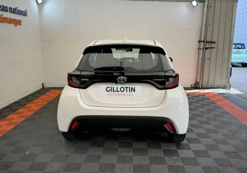 Vue arrière d'une Toyota Yaris hybride blanche de 2022 avec bande noire distinctive sur le hayon et feux arrière modernes.