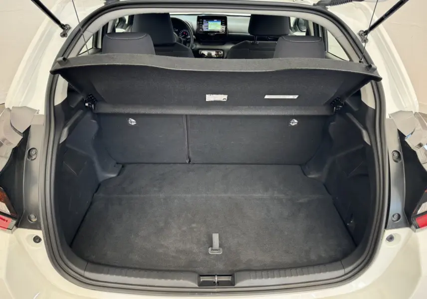 Vue arrière ouverte sur le coffre spacieux d'une Toyota Yaris hybride blanche 2022, avec intérieur noir et tablette de coffre relevée.
