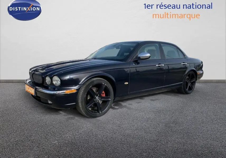 Jaguar XJ6 noir en 3/4 avant droit, avec jantes noires à cinq branches et étriers de frein rouges visibles.