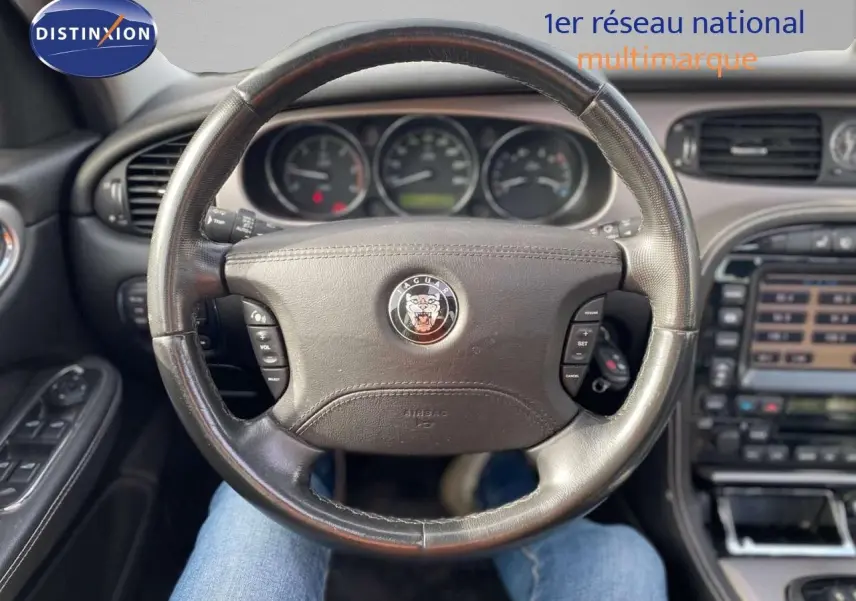 Vue intérieure centrée sur le volant en cuir noir de la Jaguar XJ6 2.7 V6 Biturbo, avec tableau de bord et commandes visibles.