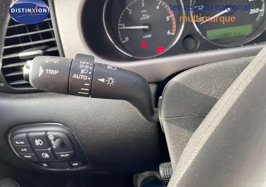 Gros plan sur la manette de clignotant et tableau de bord de la Jaguar XJ6 noire, affichant le compteur et commandes.