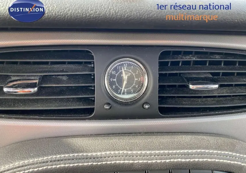 Gros plan sur l'horloge centrale et les aérateurs du tableau de bord de la Jaguar XJ6 noire de 2006.