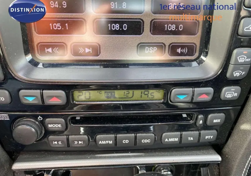 Gros plan sur la console centrale noire de la Jaguar XJ6 2.7 V6 Biturbo de 2006, montrant l'autoradio et la climatisation digitale.