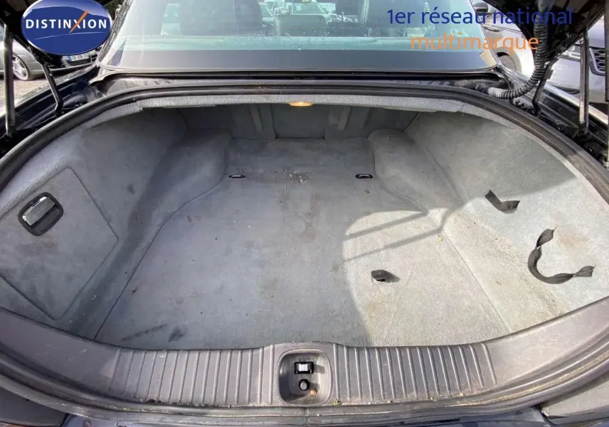 Coffre ouvert vu de l'arrière d'une Jaguar XJ6 noire de 2006, montrant un espace de rangement vide et tapissé.