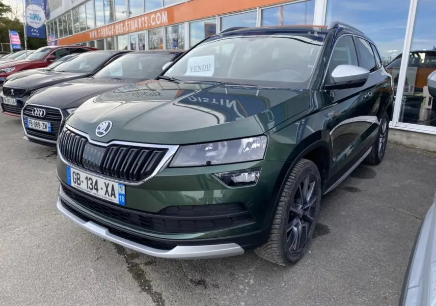 Skoda Karoq Scout vert foncé vu en 3/4 avant droit, avec jantes noires et coques de rétroviseurs blanches.