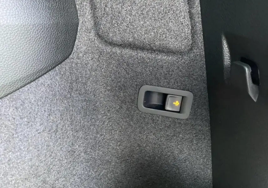 Détail du bouton de rabattement électrique des sièges dans le coffre du Skoda Karoq Scout vert foncé, vue intérieure.