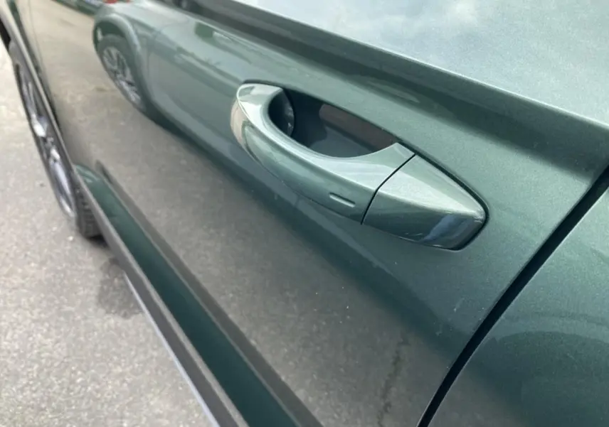 Gros plan sur la poignée de porte côté gauche d’un Skoda Karoq Scout vert foncé 2021, reflet sur la carrosserie.