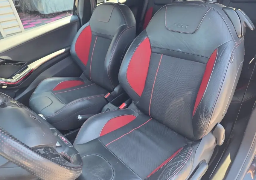 Vue intérieure côté gauche montrant les sièges baquets cuir et alcantara noirs et rouges avec logo GTI sur Peugeot 208 GTI.