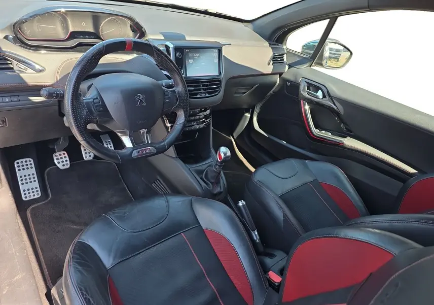 Vue intérieure côté conducteur de la Peugeot 208 GTI 2015 avec sellerie cuir noir et rouge, volant sport et levier de vitesse manuel.