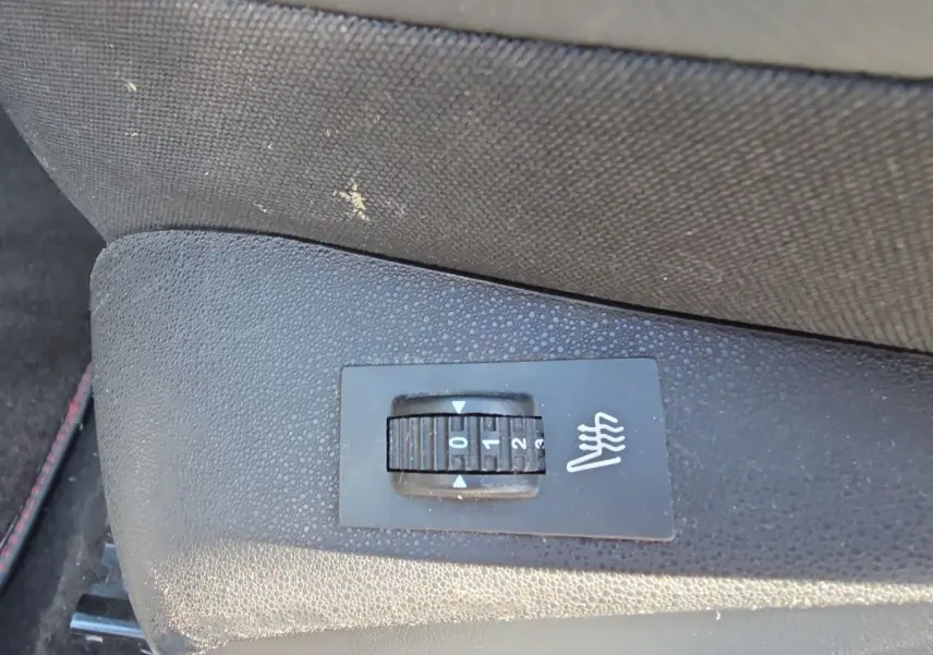 Gros plan sur le bouton de réglage des sièges chauffants noirs dans une Peugeot 208 GTI 2015.